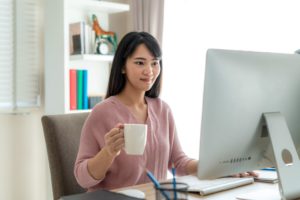 Woman sitting at desk in front of computer with cup of coffee