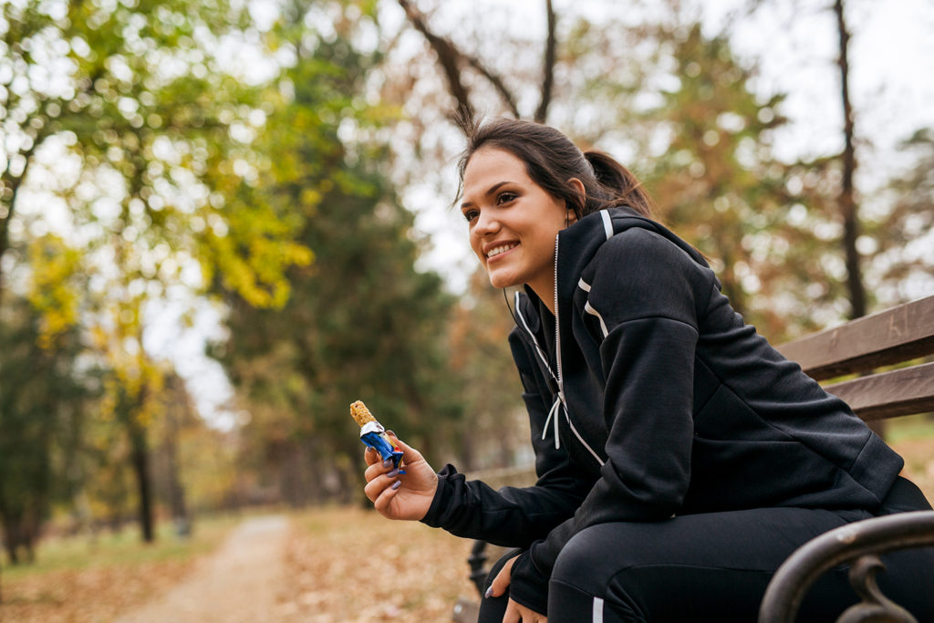 sports woman eating granola bar in city park