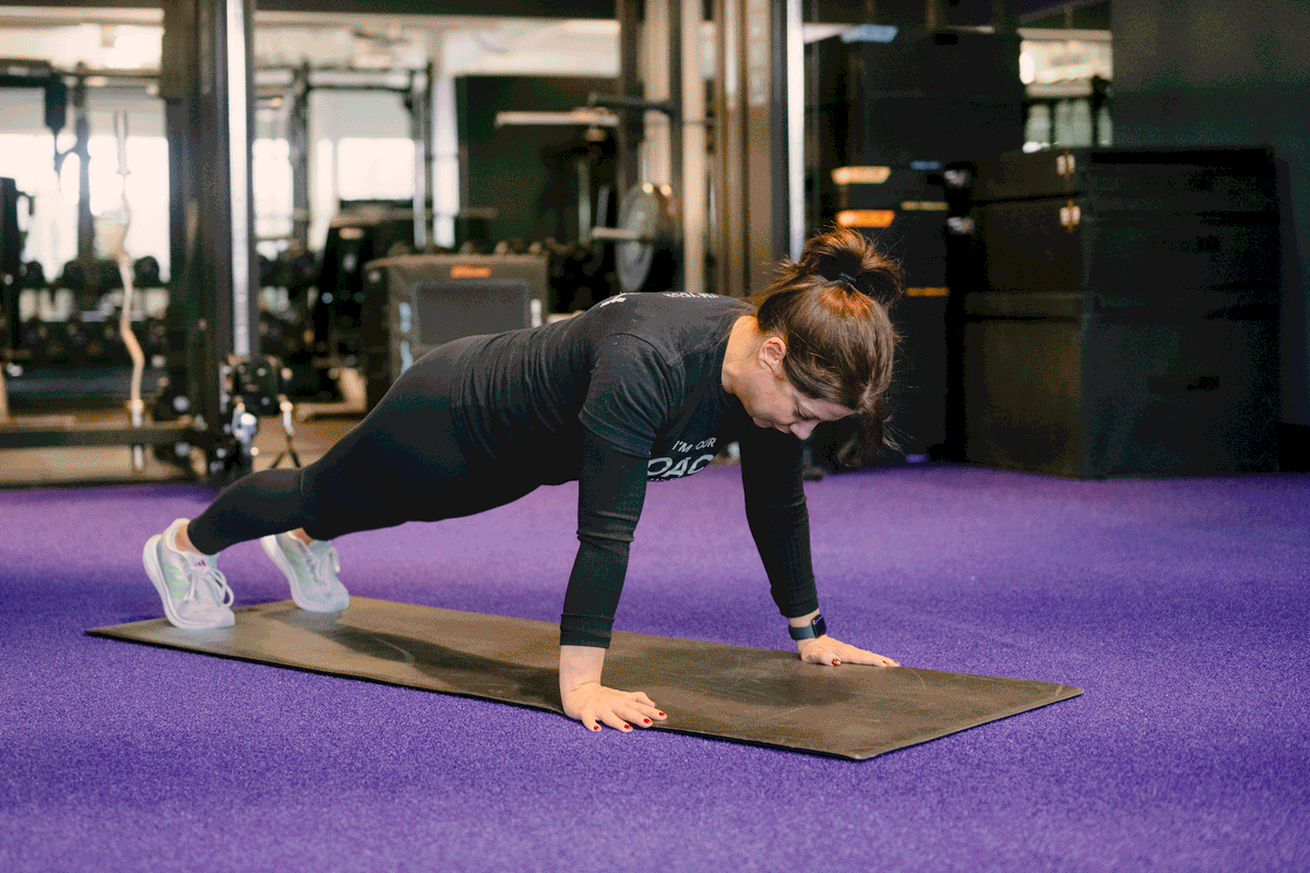 A fitness coach performing a push-up on a yoga mat, emphasizing upper body and core strength in a functional training routine.