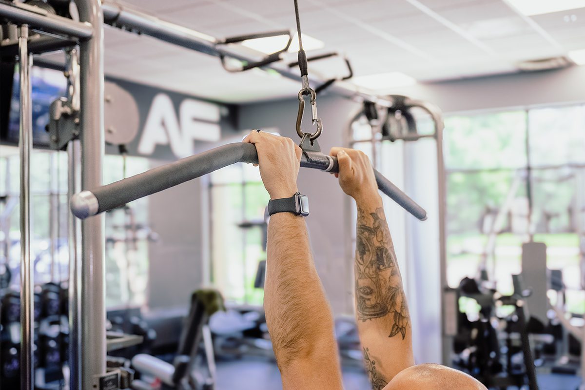 Close-up of Coach Mike demonstrating a close grip on the lat pulldown bar in a gym.
