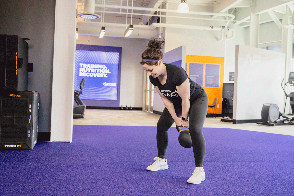 Coach Heather demonstrating a kettlebell swing in a gym setting.