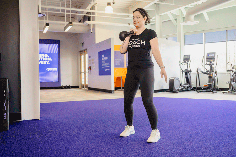 Coach Heather demonstrating a single-arm kettlebell swing clean in a gym setting.