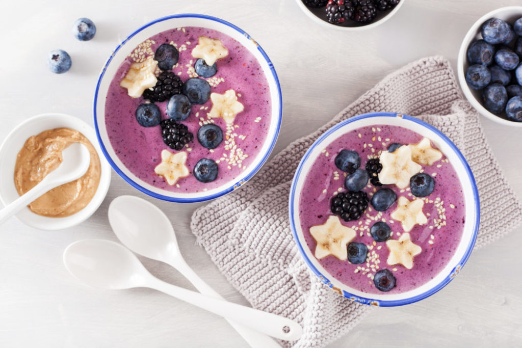 Two blueberry smoothie bowls topped in seeds and fruit.