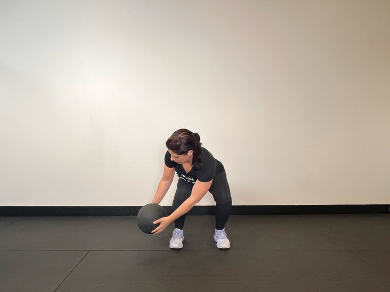 Coach in squat position, holding medicine ball outside of right foot.