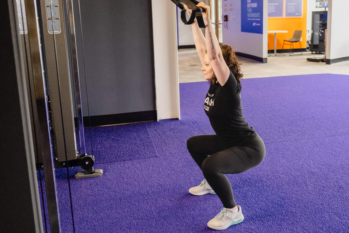 Coach Heather demonstrating an overhead squat with TRX straps.