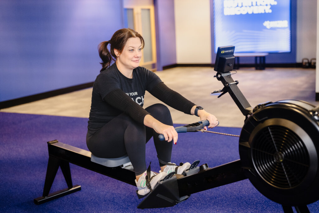 Woman performing a rowing workout on an indoor rowing machine at Anytime Fitness gym, showcasing proper rowing form and focused fitness training.