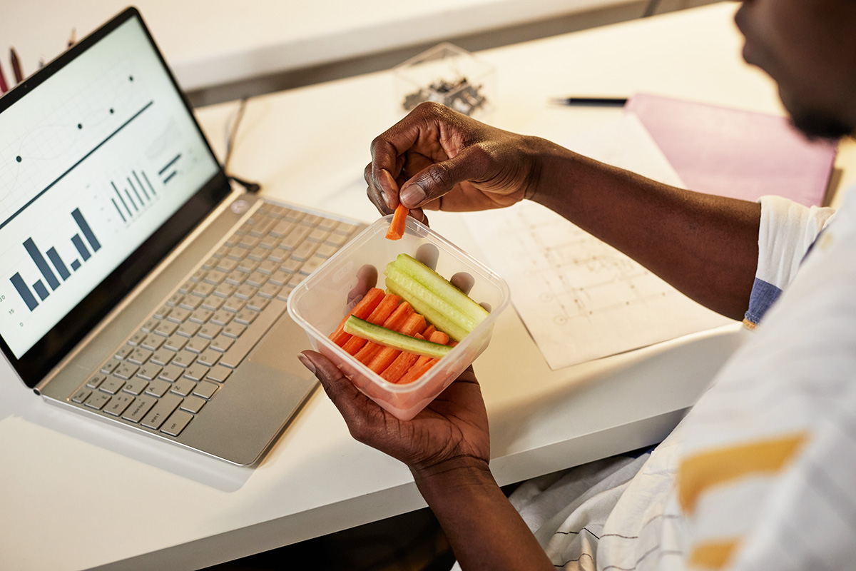 Man working at a desk and snacking on sliced carrots and cucumbers.