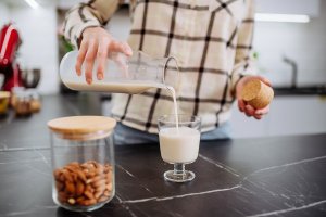 A woman pouring almond milk into a glass in kitchen. Healthy vegan product concept.