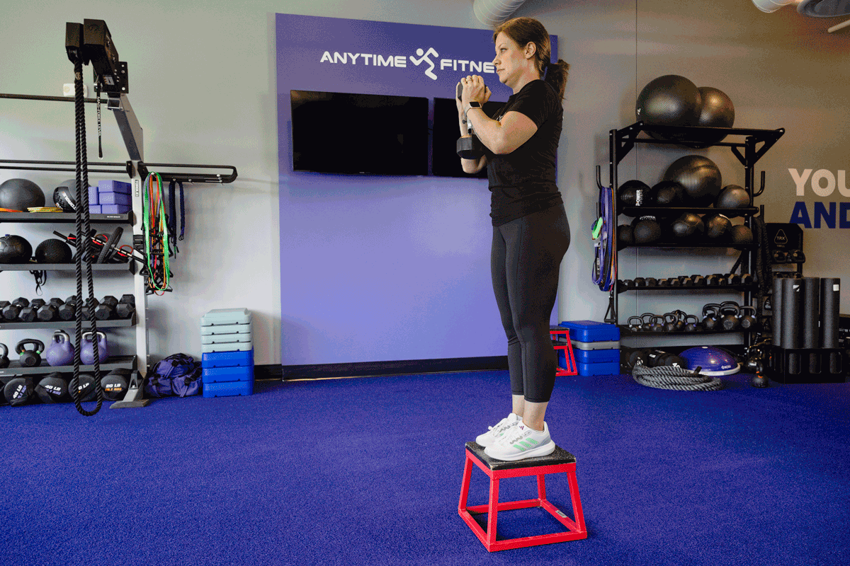 Woman performing a step-up exercise with a dumbbell onto a red box in the Anytime Fitness gym, focusing on lower body strength.