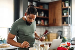 Man in his kitchen cooking while holding a tablet.