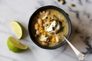 Bowl of white chicken chili next to two lime wedges