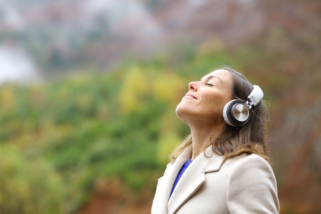 Woman standing outside with headphones in, eyes closed and head pointed towards the sky.
