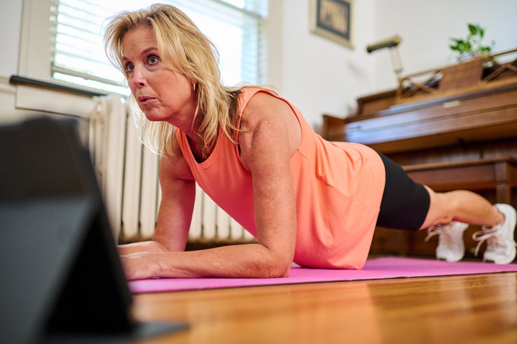 Person performing a plank exercise at home on a yoga mat, participating in a virtual fitness session for core strength and home workouts.