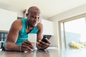 Man enjoying a smoothie after a workout while scrolling his phone.