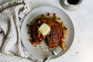 Plate with partly eaten stack of pumpkin pancakes topped in butter, syrup and pecans.