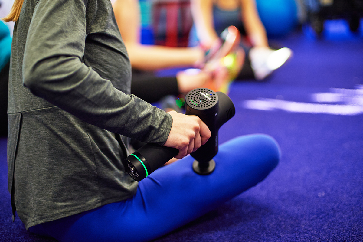 Person using a massage gun on their leg muscles after a workout, promoting muscle recovery and post-workout relaxation.