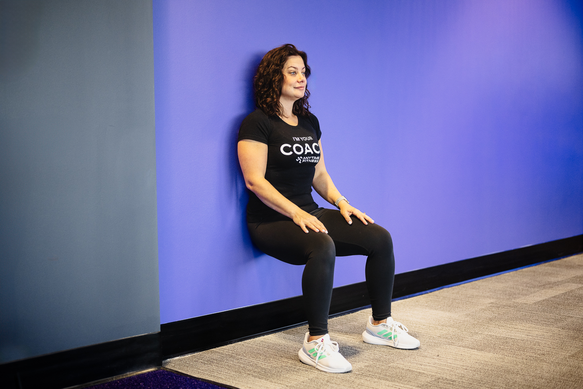 Female fitness coach executing a bodyweight wall sit exercise, focusing on leg strength and endurance. Ideal for those looking to build lower body stability and core strength.