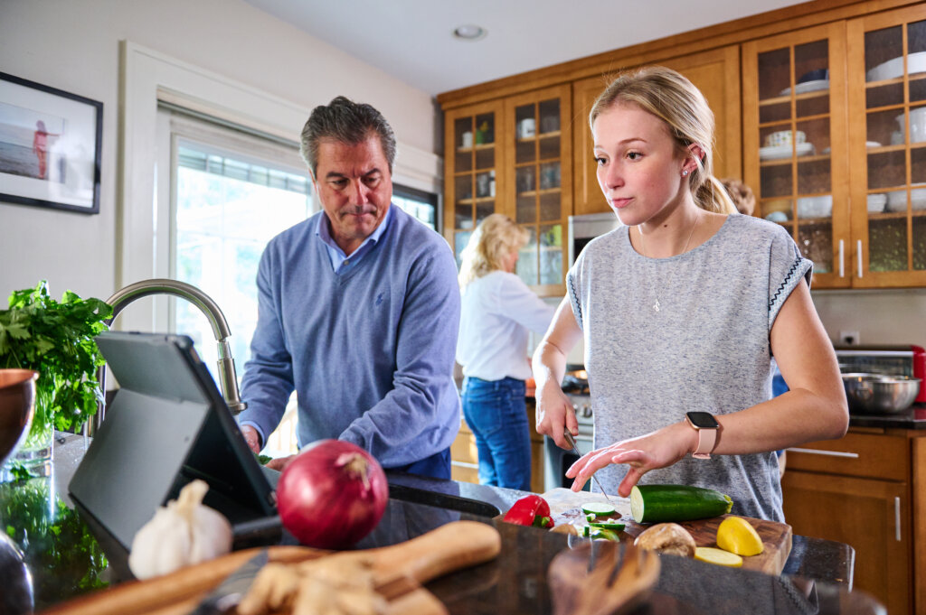 Young woman prepping vegetables in the kitchen while older male uses kitchen sink.