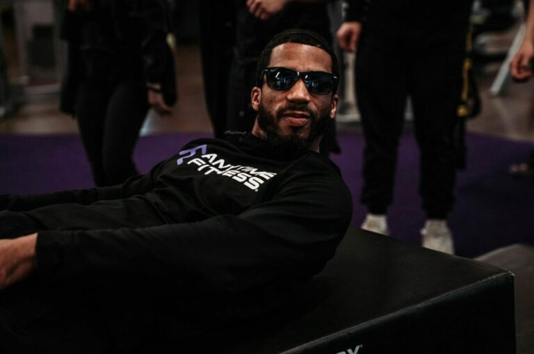 Coach wearing sunglasses is reclining on a bench in a dimmed room.