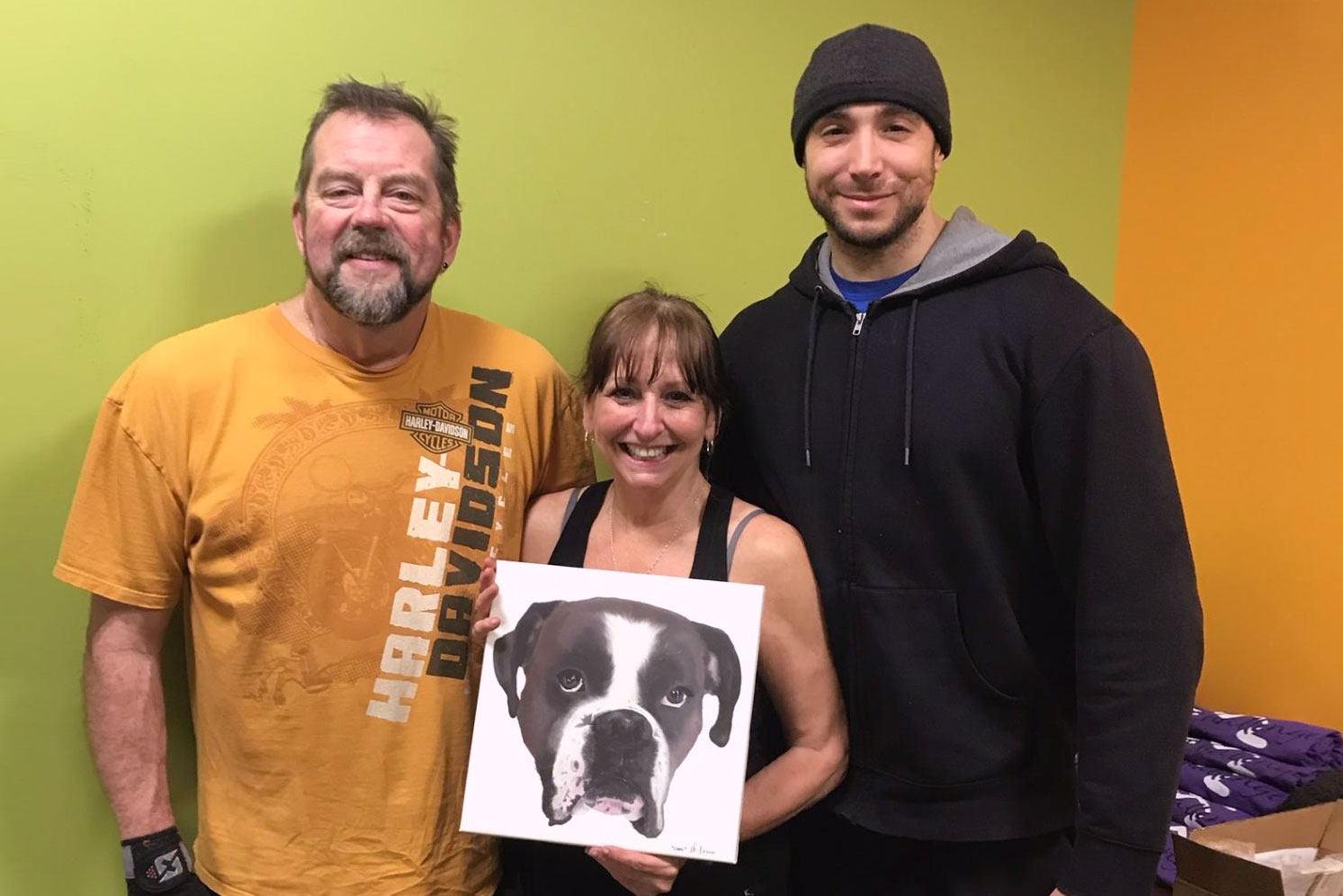 Jaymie posing with her husband, Ralph, and trainer, Daniel, holding a large photo of her dog.