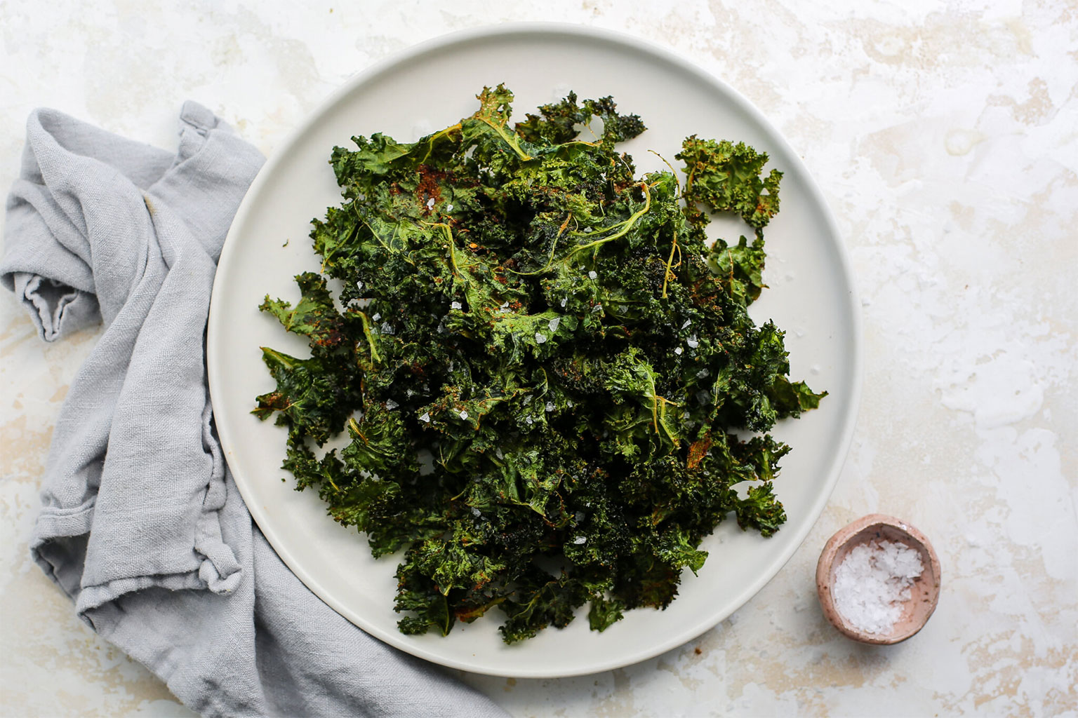 White plate with crispy kale chips seasoned with sea salt.