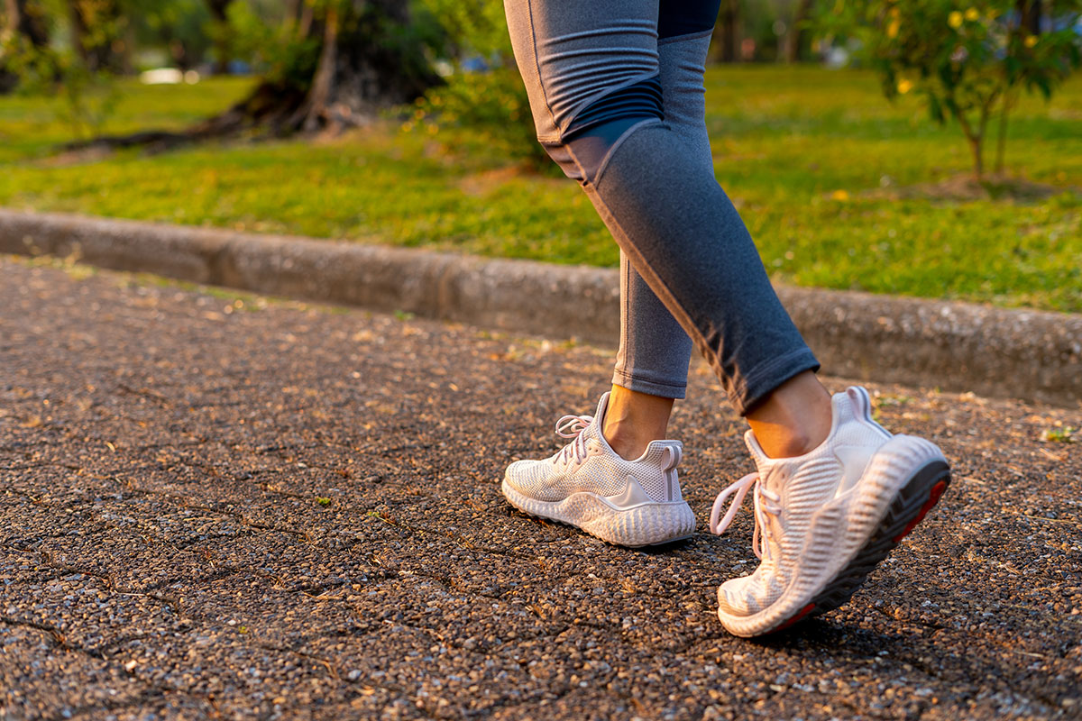 Close-up of a person’s feet in athletic shoes walking on a paved path, demonstrating the physical benefits of taking daily walks.