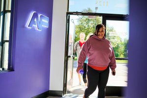 Woman in sweatshirt entering an Anytime Fitness gym.