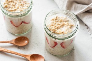 Two glass jars filled with overnight oats and strawberries, sitting next to two wooden spoons.