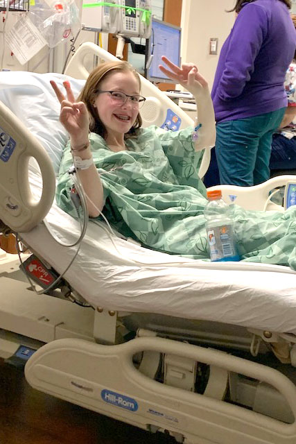 Mary’s daughter, Sara, in a hospital bed giving two peace signs.