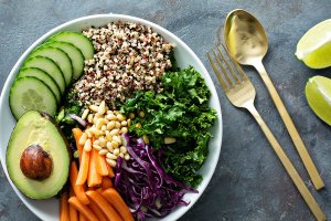 Overhead view of a grain bowl filled with quinoa, greens, avocado, carrots, seeds, and red cabbage.