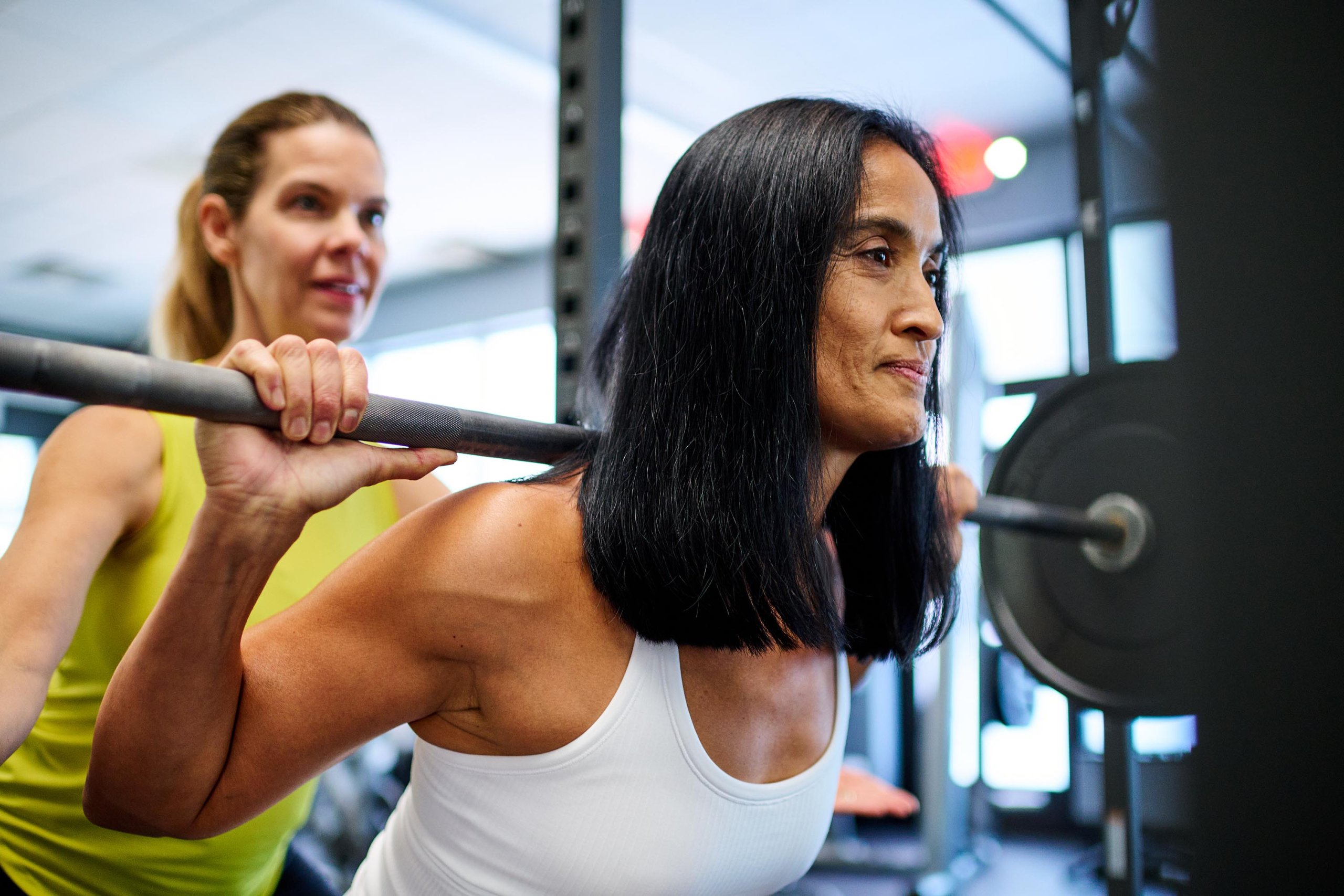 Woman practicing kettlebell squat with personal trainer at gym