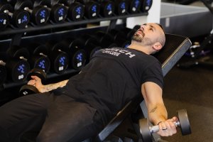 Man lying on a gym bench doing the incline dumbbell fly.