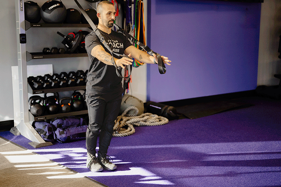 Anytime Fitness Coach Mike demonstrating a TRX forward lunge and fly in a gym setting.