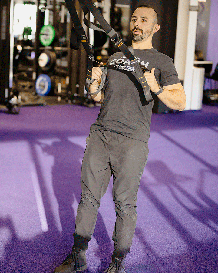 Anytime Fitness Coach Mike demonstrating a TRX squat and row in a gym setting.