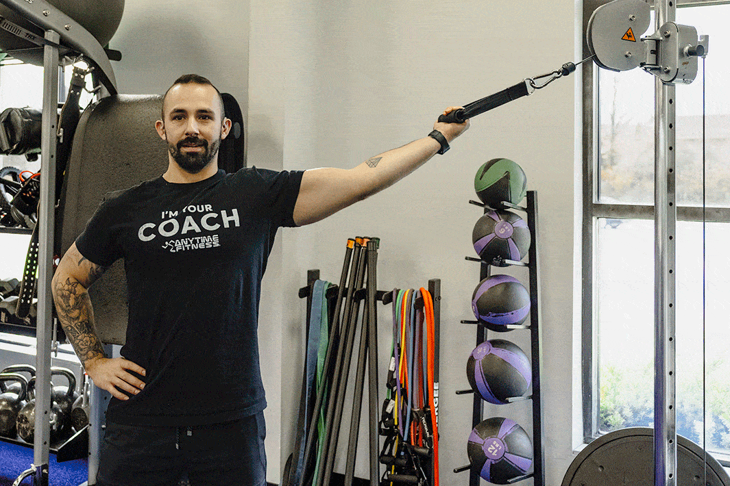 Coach Mike demonstrating a single-arm high curl with a cable attachment in a gym setting.
