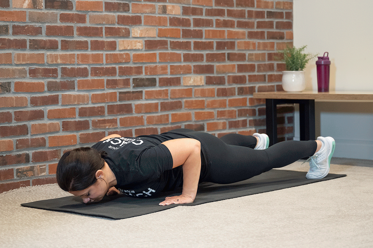 Woman doing push-ups on a yoga mat in her living room.