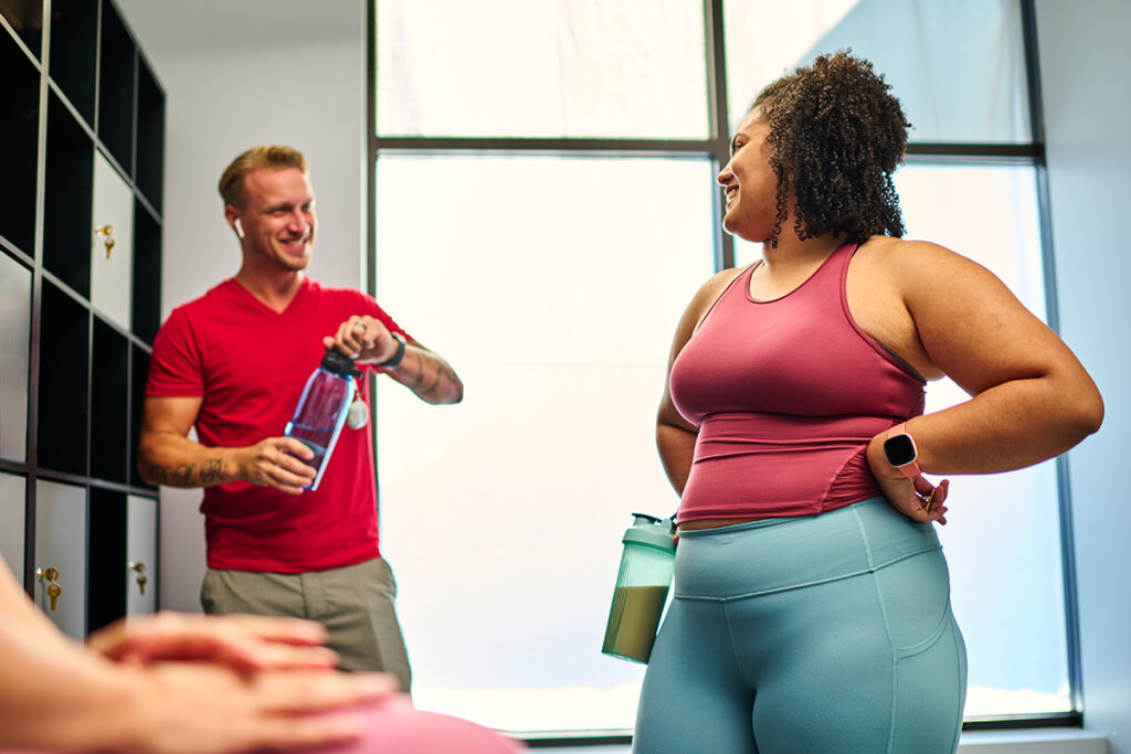 Two gym-goers chatting near lockers, holding water bottles, and preparing for their workout, highlighting pre-workout hydration and supplements.