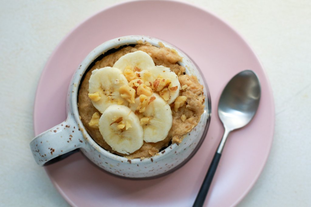 Banana and walnut topping on a completed banana bread in a mug with a spoon.
