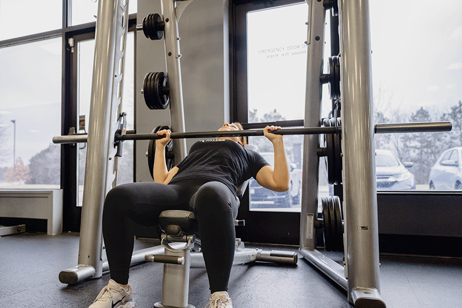 Coach Heather performing an incline chest press throw on a Smith machine while strength training in a fitness center.