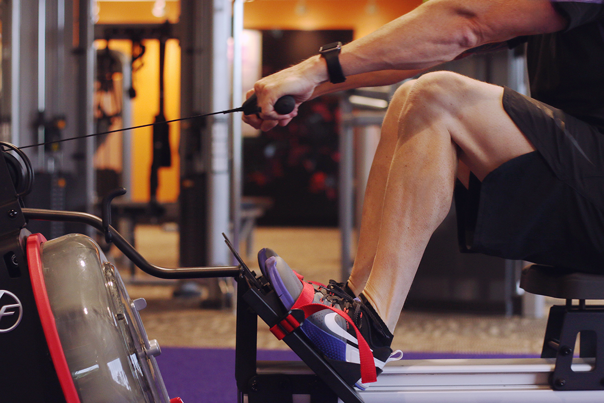 Close-up of a man’s legs and arms using a rowing machine in a gym.