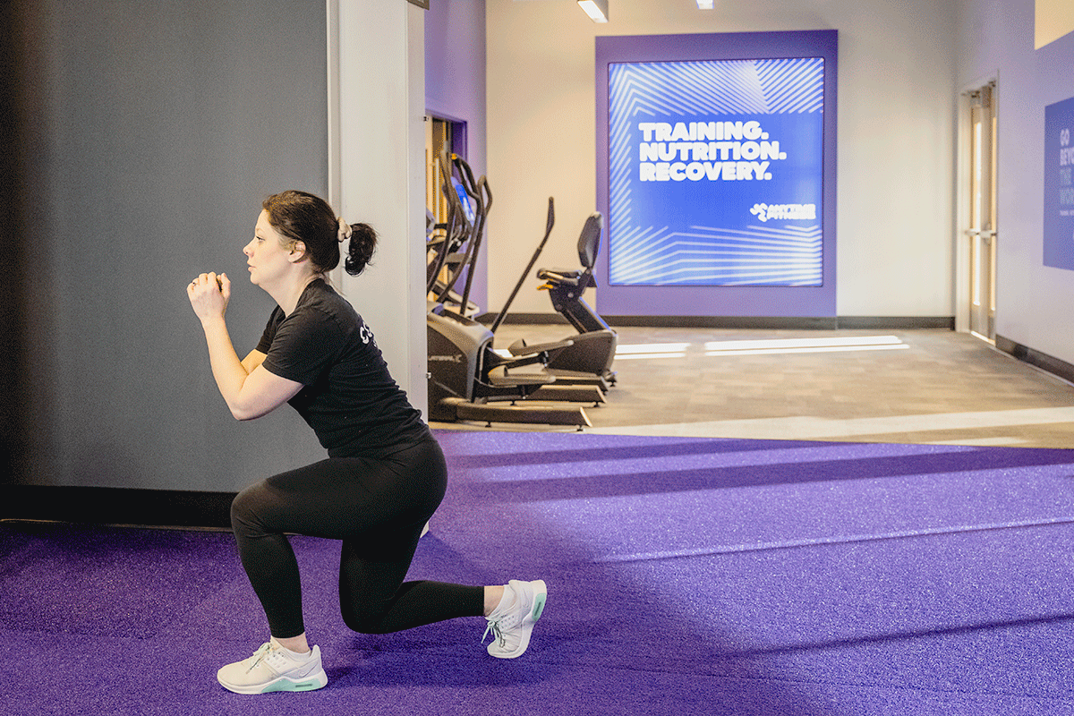 Woman in a gym bending at the hips and knees then jumping off the floor, landing in a lunge.