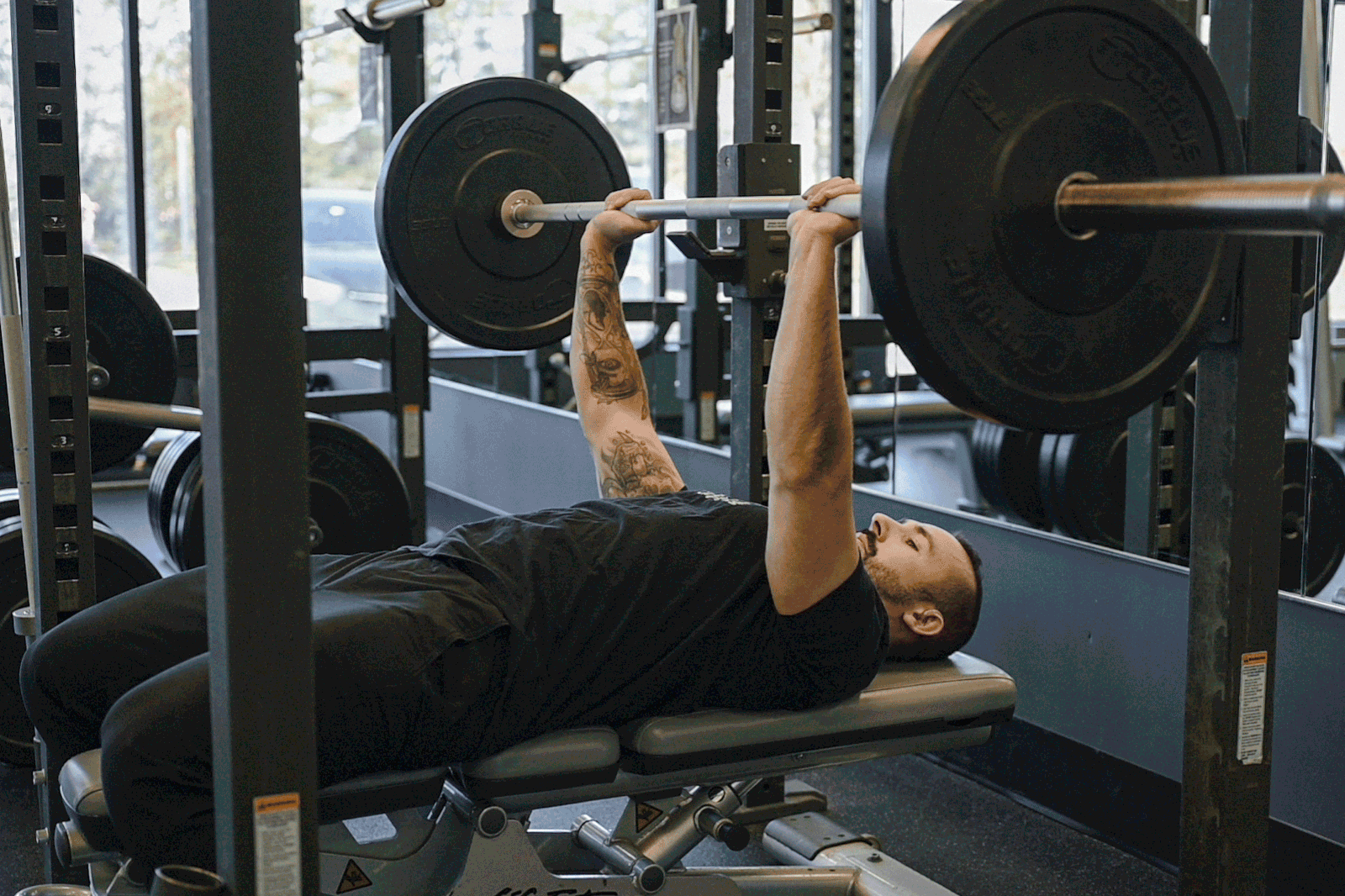 Coach Mike demonstrating a barbell bench press in a gym setting.