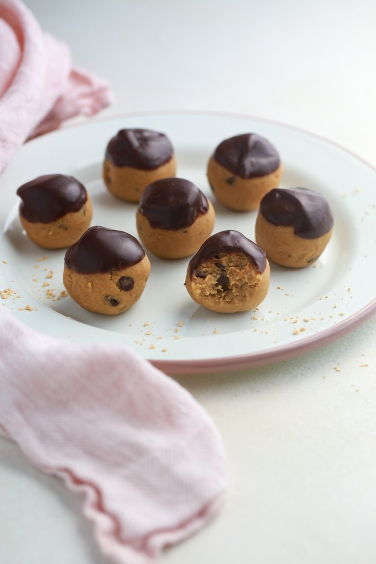 Chocolate chip cookie dough bites dipped in melted chocolate, arranged on a plate with a pink napkin nearby.