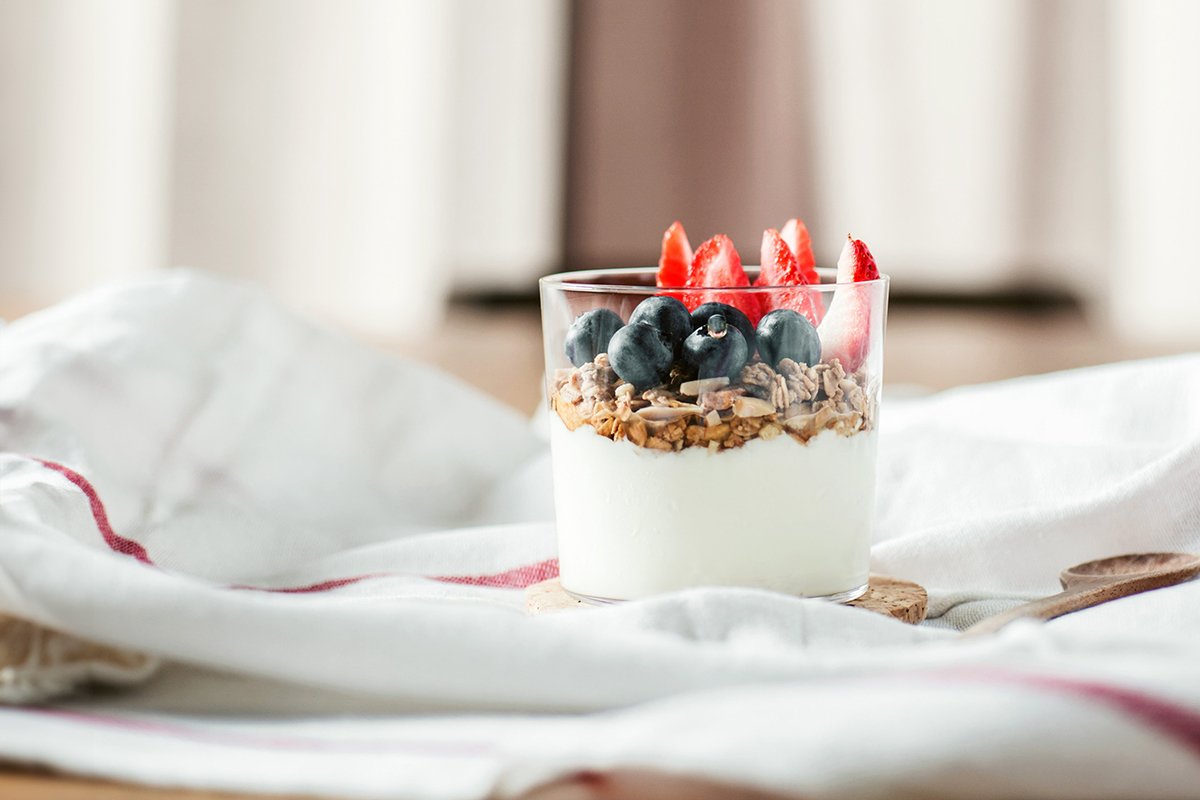 A glass full of Greek yogurt, granola, blueberries, and strawberries sitting on a white linen napkin.