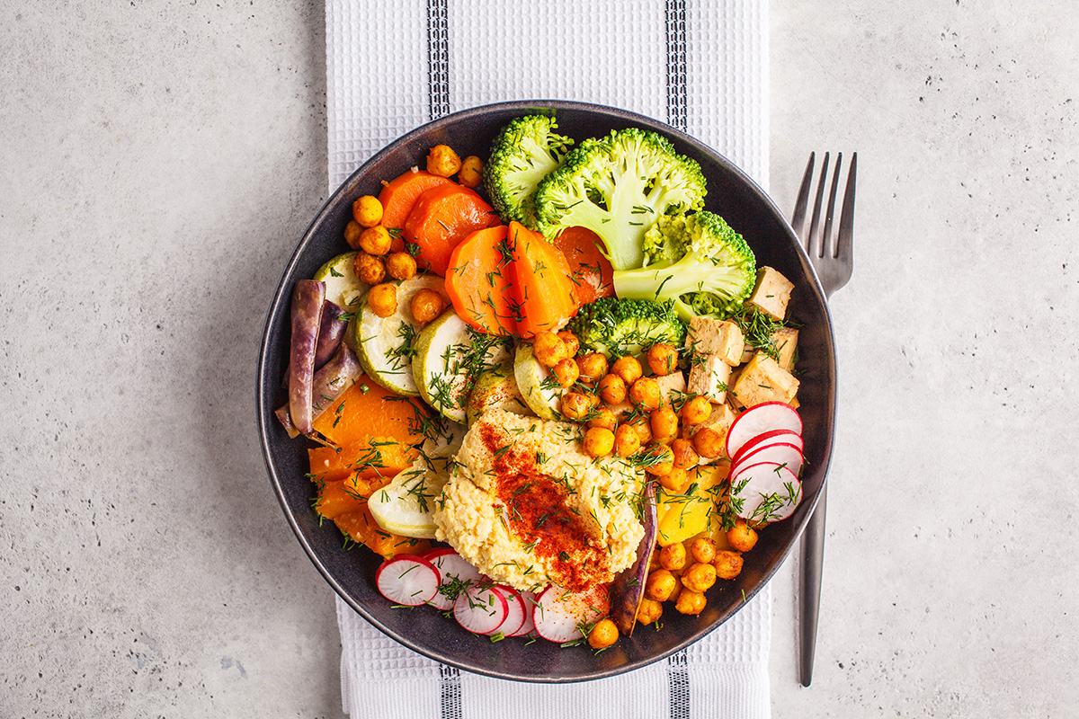 Vegan Buddha bowl with baked vegetables, chickpeas, hummus and tofu on white background.