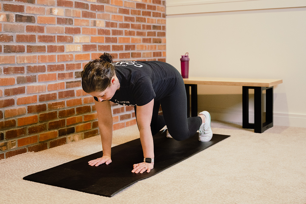 Coach Heather performs a bear plank hold on a yoga mat on the floor.