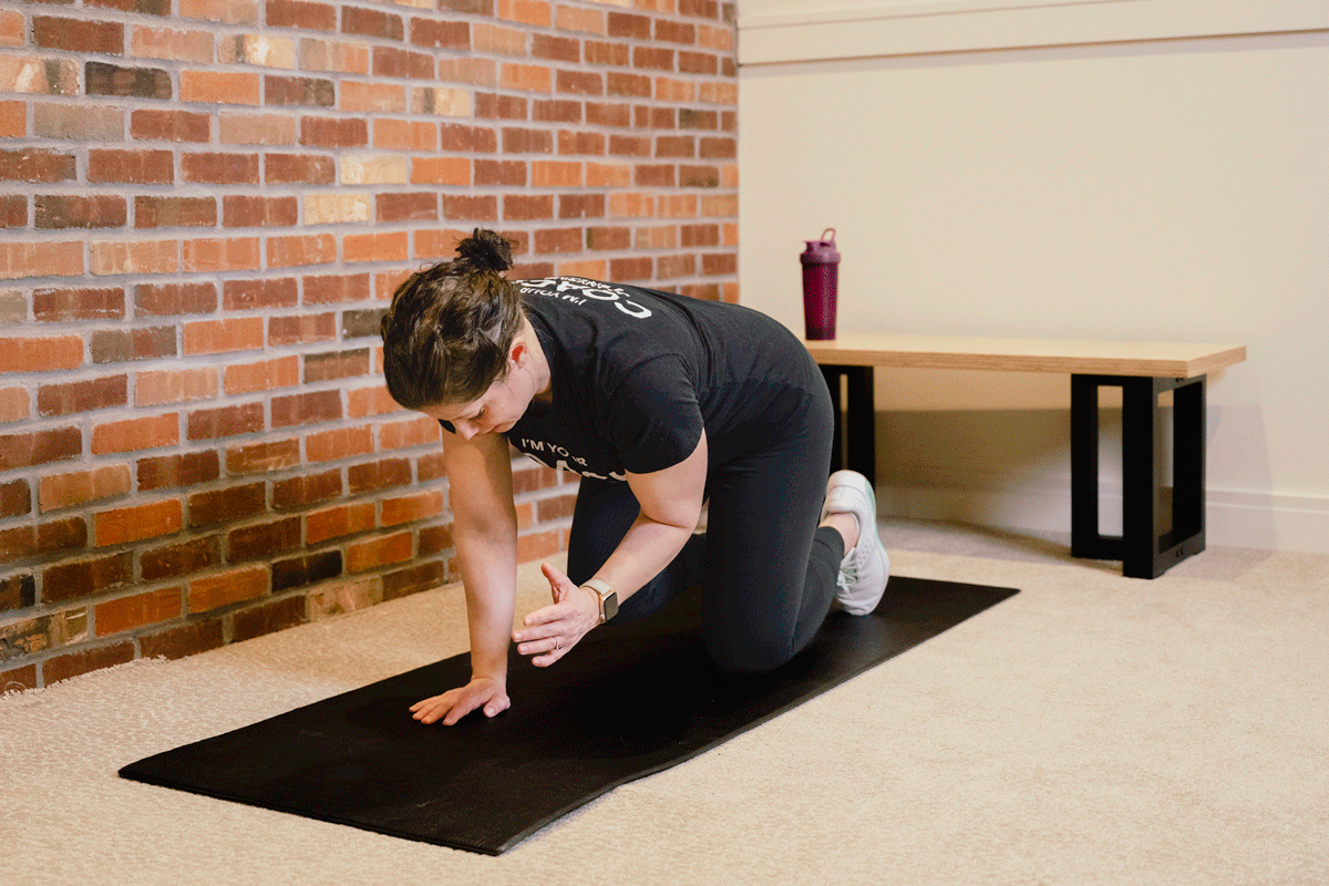 Coach Heather performs reps of a bird dog exercise on a yoga mat on the floor.