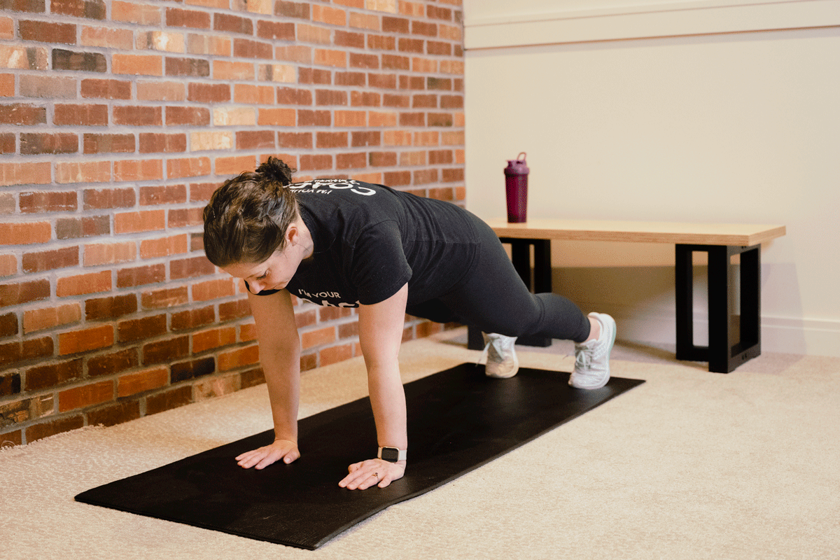 Coach Heather performs reps of plank shoulder taps on a yoga mat on the floor.