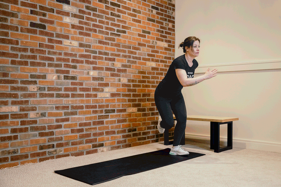 Coach Heather demonstrating skaters on an exercise mat with a bench and a brick wall behind her.