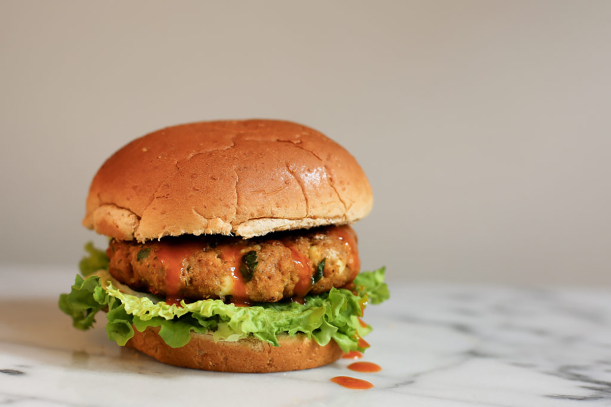 Buffalo-style turkey burger with lettuce and a whole wheat bun, topped with hot sauce, on a marble surface with a neutral background.